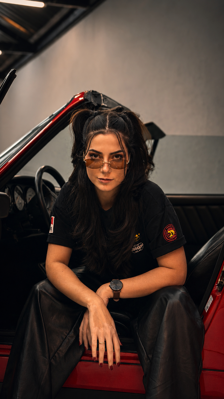 Katharina Zaparoli sentada na porta de um carro clássico vermelho
